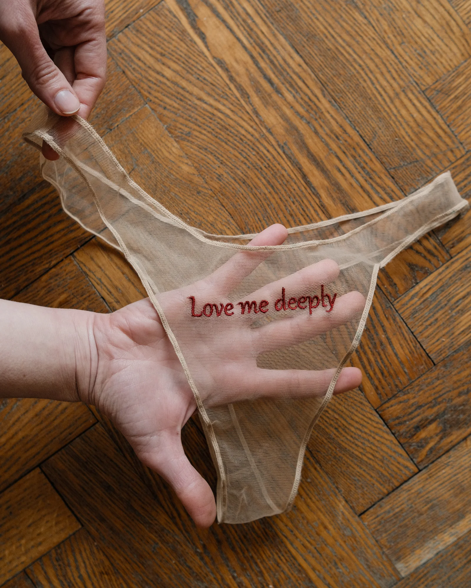 Transparent embroidered panties held over a wooden floor